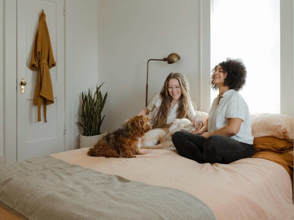 Two women sitting on a bed with their dogs