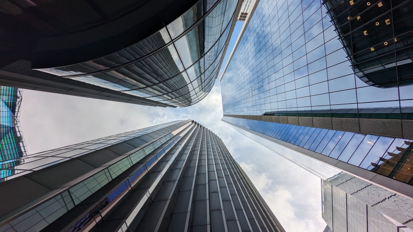 Looking up at a group of skyscrapers in central London. The sky and the clouds are in the background.